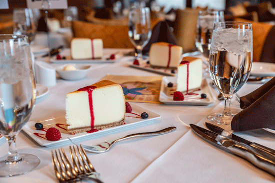 A photo of a table with a white tablecloth and several cheesecakes with red fruit syrup.
