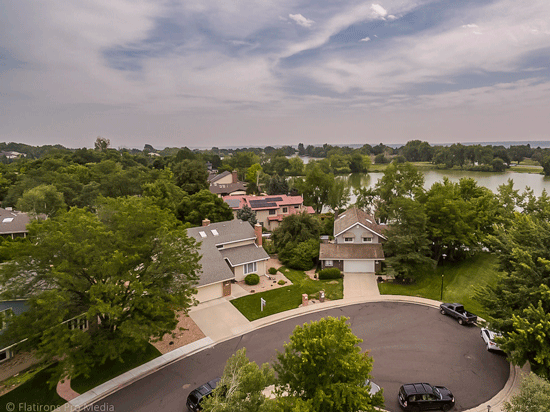 An aerial photo of a suburban cul-de-sac with many vehicles and two visible driveways and many trees surrounding the houses.