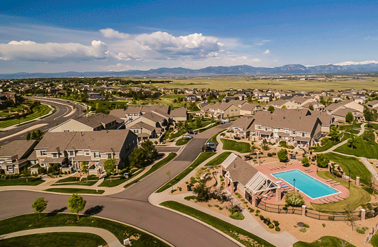 An aerial photo of a suburban neighborhood with a mountain range in the background and a pool to the right.