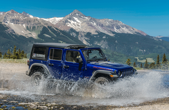 A photo of a blue jeep driving through water with a mountain range in the background.