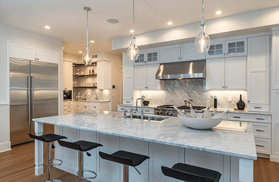 A photo of a kitchen with brushed steel accents and a marble-topped kitchen island with black barstools.